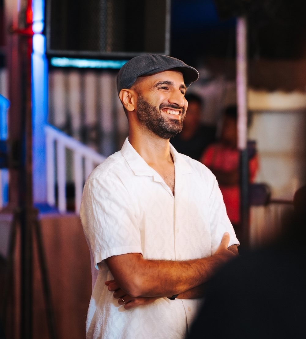 Frank Lobo, smiling, standing in a room of people at an evening gathering.